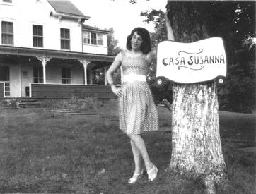 A photograph of Susanna Valenti posing with the sign of her Catskills resort and transvestite getaway, Casa Susanna.